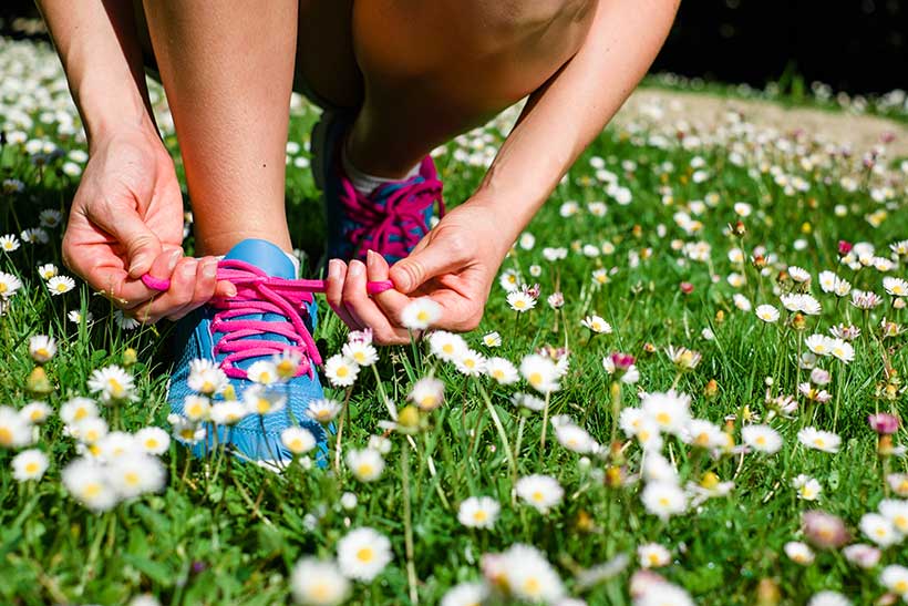 Ein Läufer bindet sich auf einer Frühlingswiese die Laufschuhe zu.
