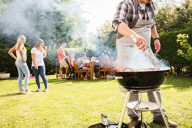 Mehrere Personen stehen zum Grillen in einem Garten.