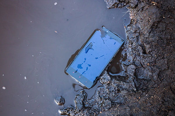 Ein Smartphone liegt in einer schlammigen Pfütze.