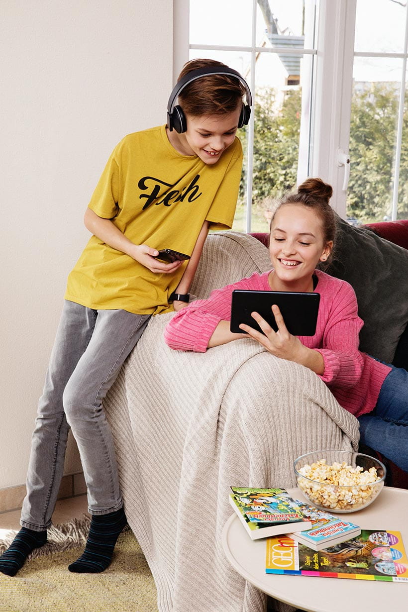 Junge und Mädchen sitzen mit Smartphone und Tablet im Wohnzimmer